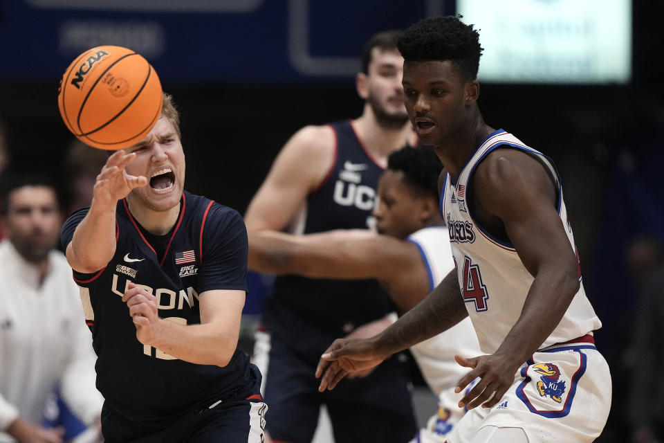 UConn guard Cam Spencer, left, passes around Kansas forward K.J. Adams Jr. during the first half of an NCAA college basketball game Friday, Dec. 1, 2023, in Lawrence, Kan. (AP Photo/Charlie Riedel)