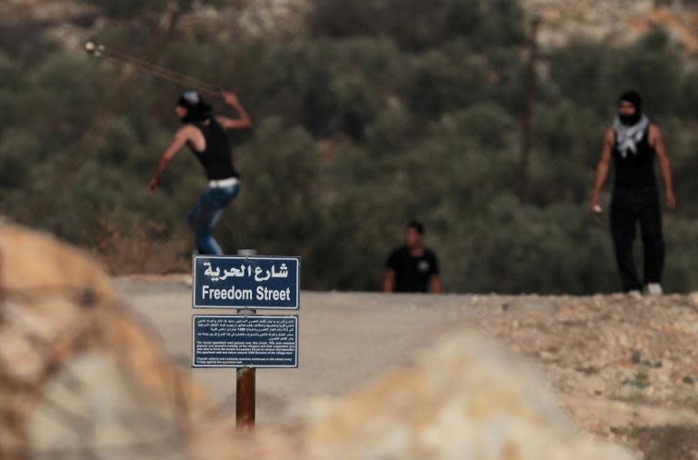 A placard that reads in Arabic and English "Freedom Street" is seen as Palestinian protesters throw stones towards Israeli security forces in the West Bank village of Bilin, West of Ramallah, on November 15, 2013