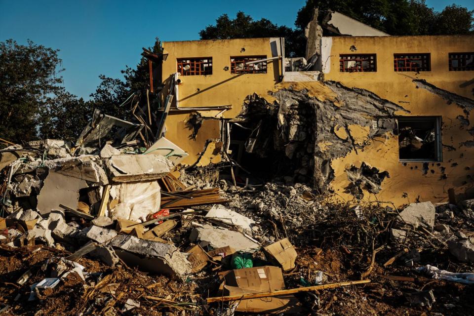 A large pile of rubble next to a scarred yellow building with no roof and a large hole in one wall