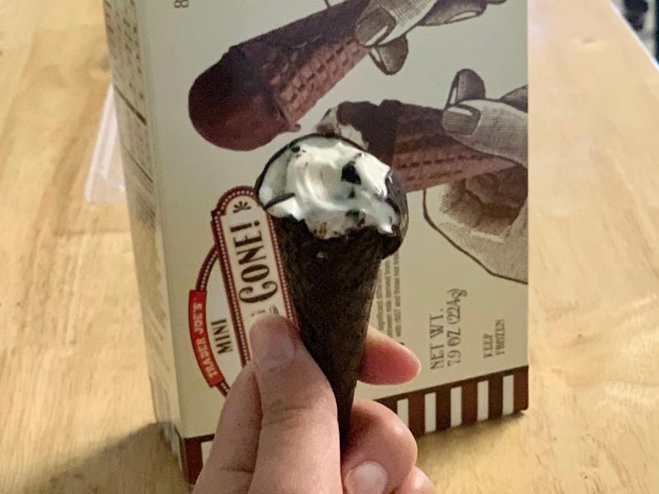 A hand holding a small chocolate ice-cream cone with the original Trader Joe's Hold the Cone packaging in the background