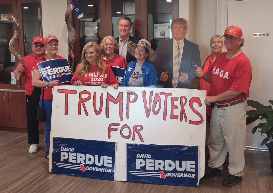 Former Republican Sen. David Perdue of Georgia, standing behind a crowd of supporters, a cardboard cutout of former President Donald Trump to his immediate right, poses for a photo in front of homemade sign that reads "Trump Voters for David Perdue" during a campaign stop in Augusta, Georgia on Friday, May 20.