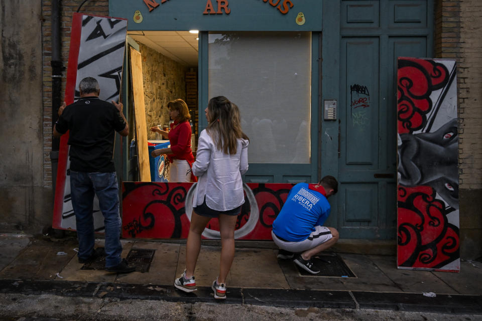 A group of people protect the entrance of a local business before the first day of the running of the bulls during the San Fermin fiestas in Pamplona, Spain, Friday, July 7, 2023. (AP Photo/Alvaro Barrientos)