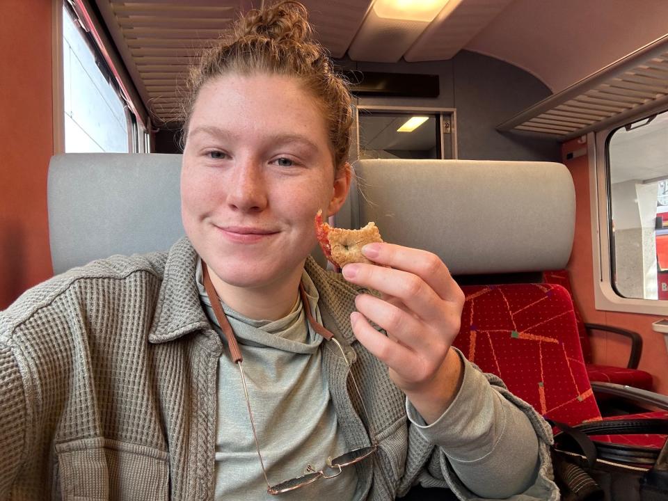 selfie of the author sitting in a train seat smiling and holding up a small cookie tart