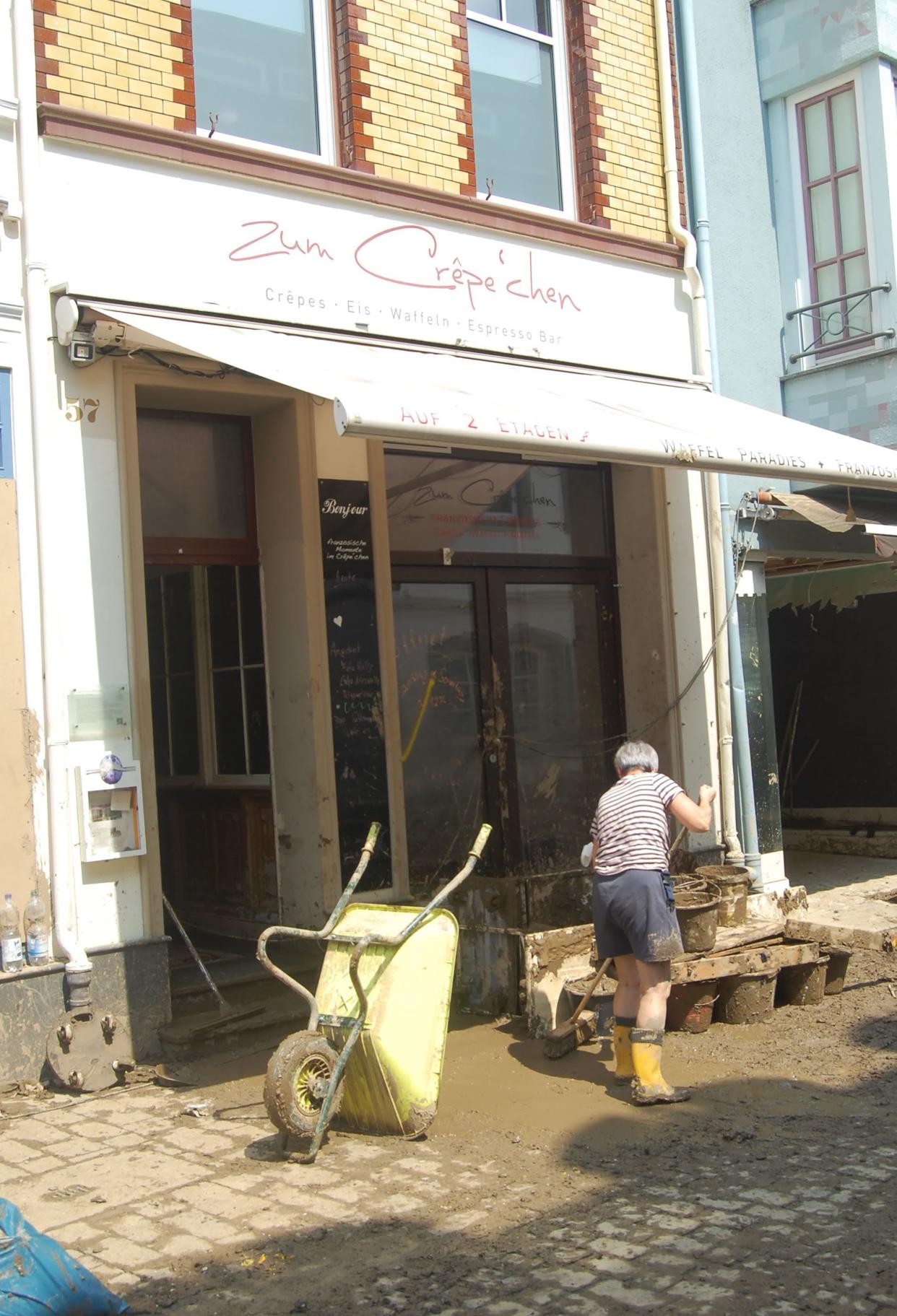 A woman uses a broom to sweep mud away from the entrance of a small restaurant in Ahrweiler, Germany.