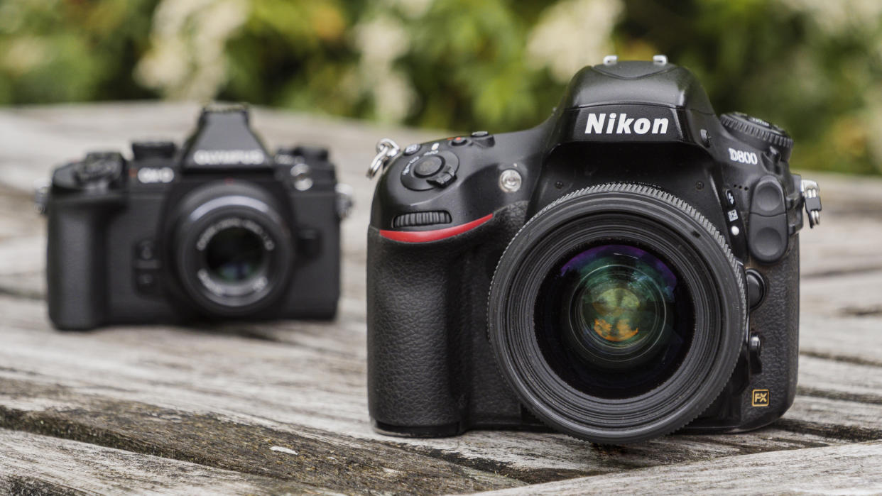  Two cameras sitting next to each other on a wooden table. 