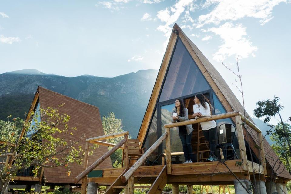 Two women stand outside on the balcony of an A-frame house on a beatuiful clear dat. 