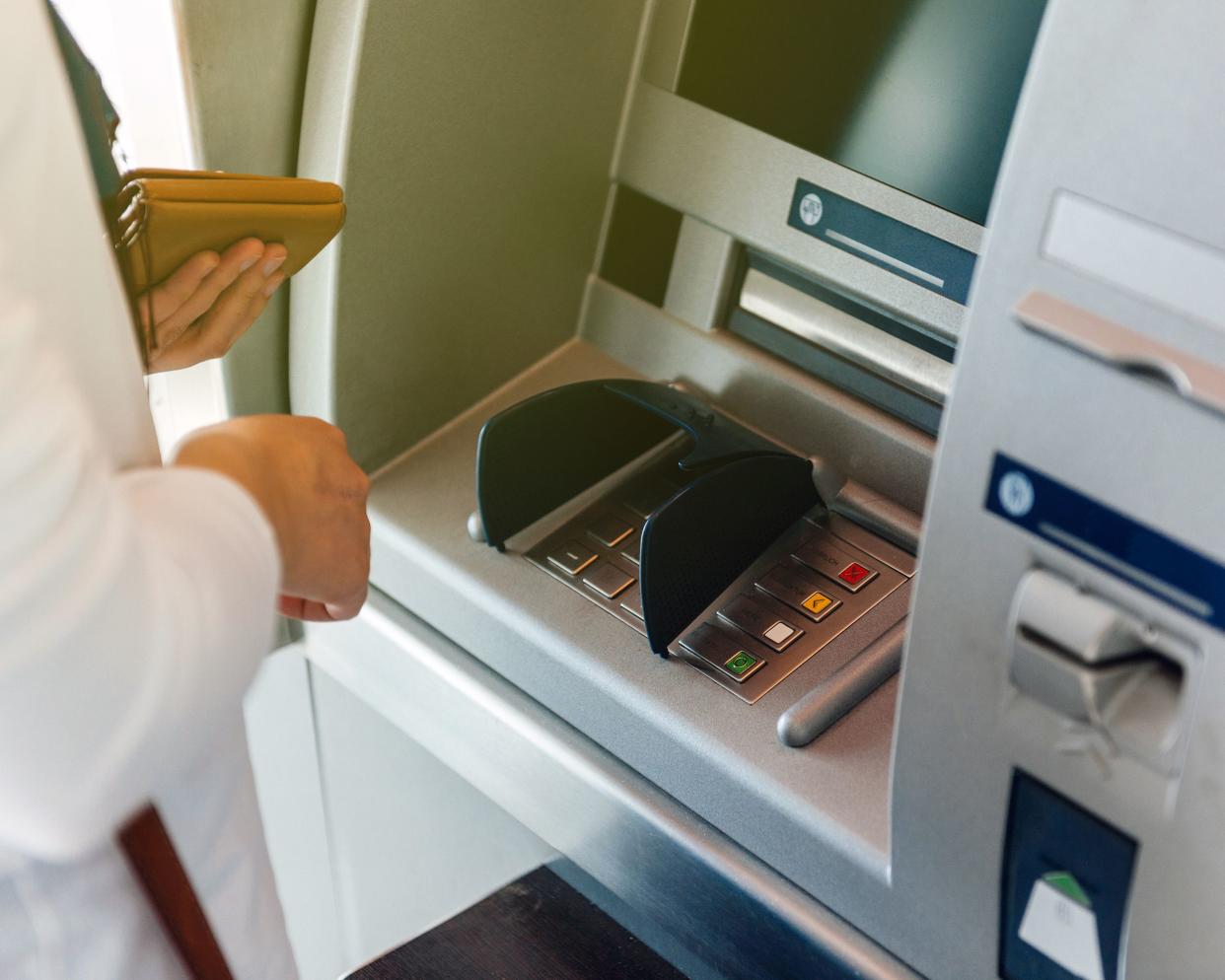 side view of woman using ATM holding wallet an pressing the PIN