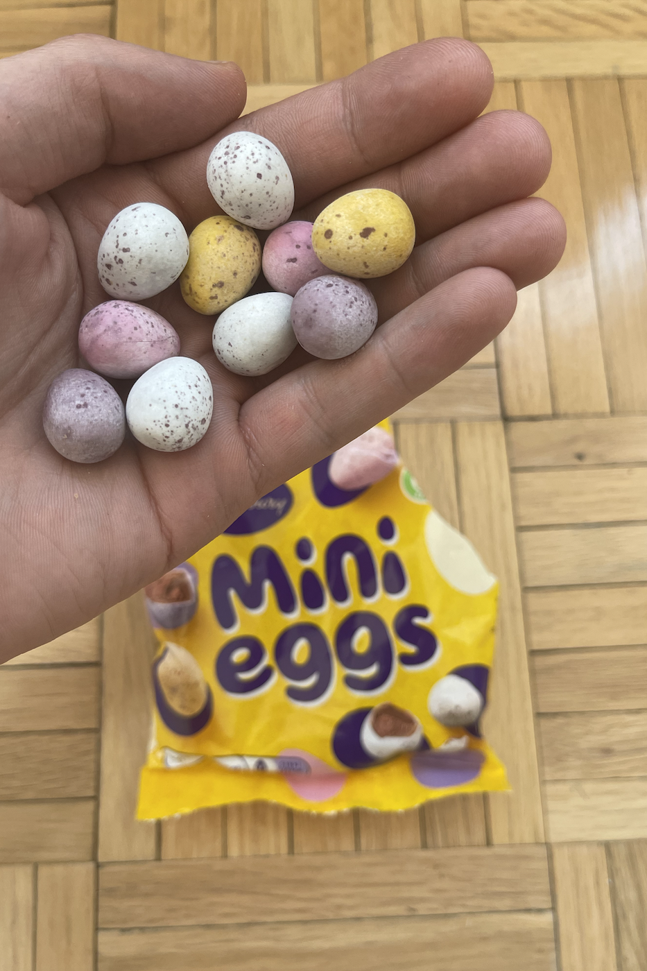 Hand holding various mini candy eggs above an open Mini Eggs candy package