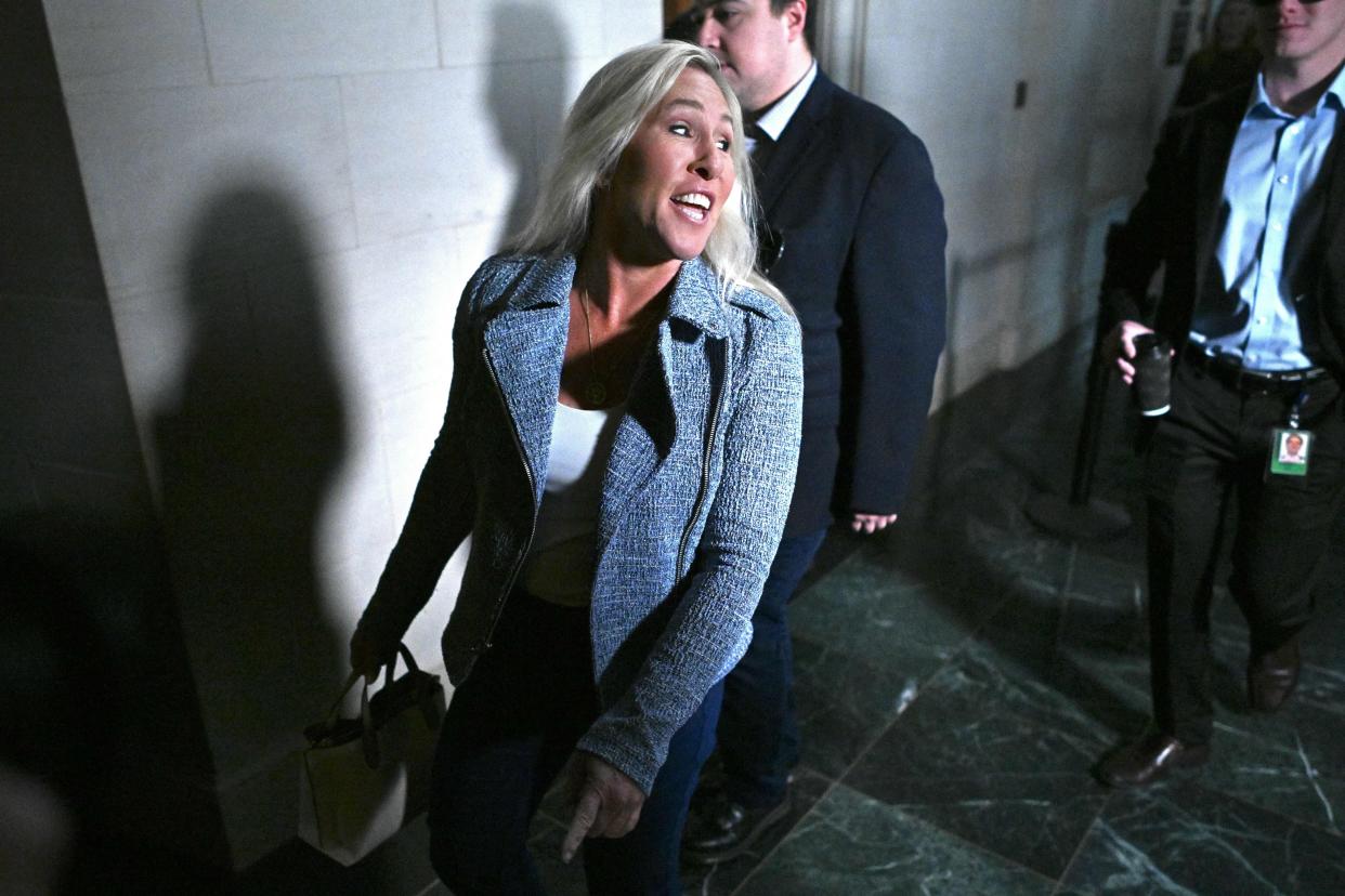 A gleeful woman dressed in a business casual outfit throws her head back to talk to reporters as she walks down a hallway.