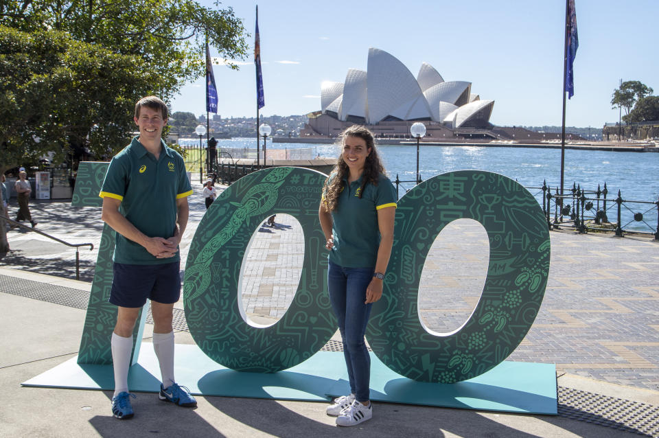 Australian Olympians Edward Fernon, modern pentathlon, and slalom canoeist Jess Fox stand by a sign at a ceremony to mark 100 days before the start of the Tokyo Olympics in Sydney Wednesday, April 14, 2021. Olympics live sites will be held across Australia during the Olympic Games, from July 23 to Aug. 8 2021, taking advantage of the one hour time zone difference for Australians to watch athletes perform. (AP Photo/Mark Baker)