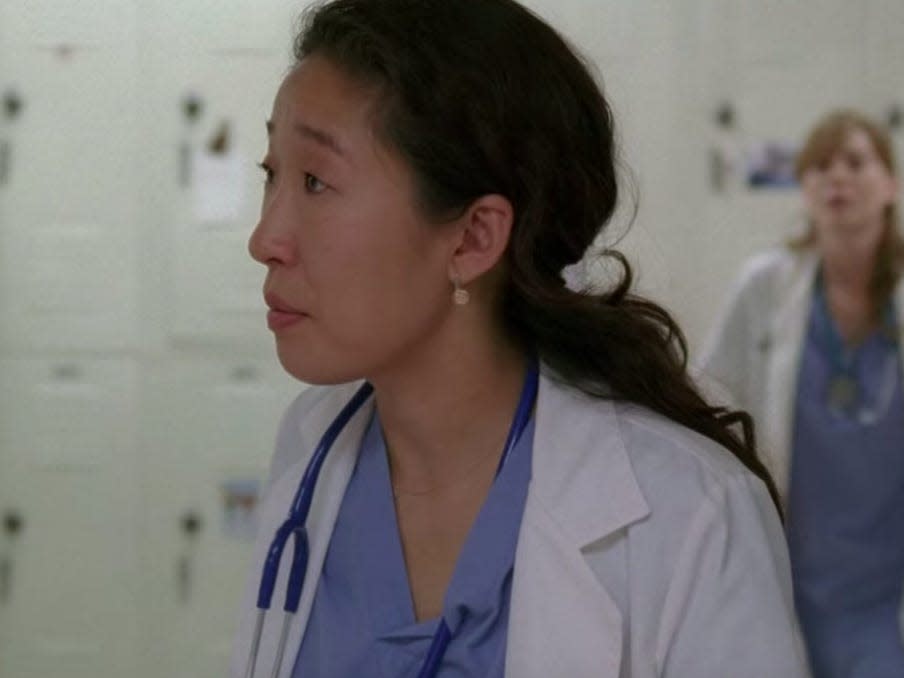 Sandra Oh as Cristina Yang on Greys Anatomy wearing blue scrubs and a coat