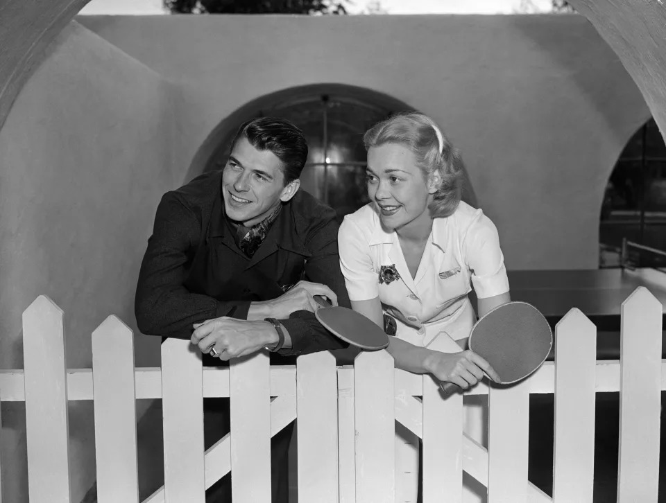 Newlyweds Ronald Reagan and Jane Wyman lean on a white picket fence, after playing ping pong during their honeymoon at El Mirador Hotel.