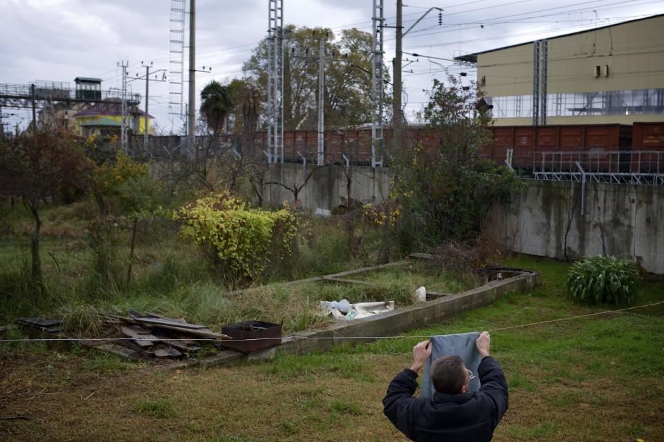 In this photo taken on Wednesday, Nov. 27, 2013, a man is hanging out a piece of cloth to dry in the yard of the 5a Akatsiy house as a freight train drives past in the village of Vesyoloye outside Sochi, Russia. As the Winter Games are getting closer, many Sochi residents are complaining that their living conditions only got worse and that authorities are deaf to their grievances. (AP Photo/Alexander Zemlianichenko)