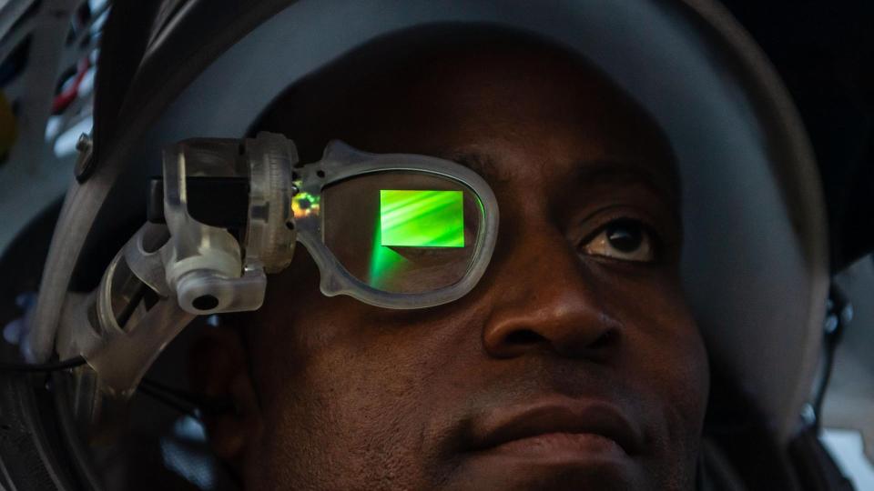     An astronaut wears a helmet with a glowing green screen in front of his right eye. 