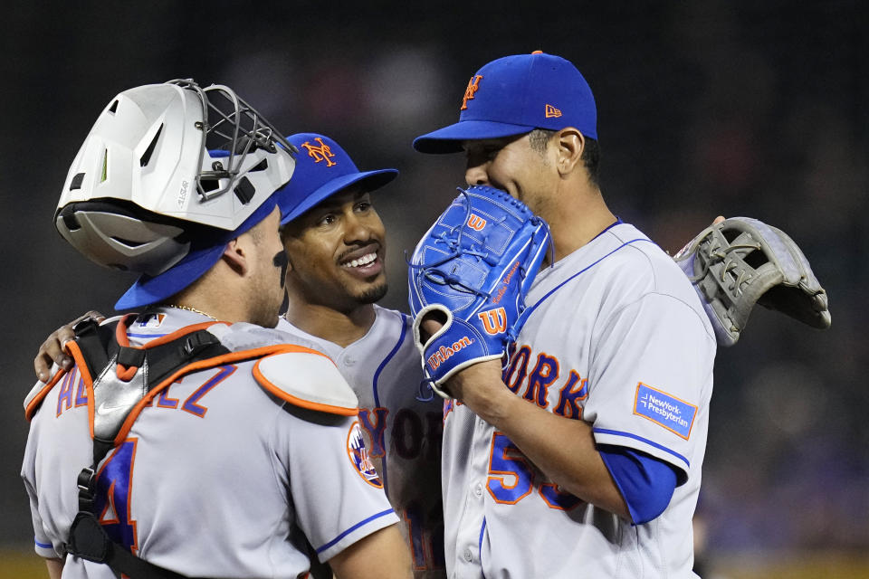 New York Mets shortstop Francisco Lindor, middle, smiles as he talks with starting pitcher Carlos Carrasco, right, and catcher Francisco Alvarez during the fourth inning of the team's baseball game against the Arizona Diamondbacks on Thursday, July 6, 2023, in Phoenix. (AP Photo/Ross D. Franklin)