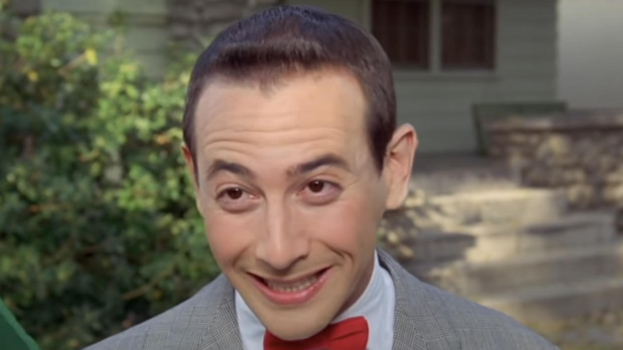  Paul Reubens grinning outside as Pee Wee Herman in Pee Wee's Big Adventure. 