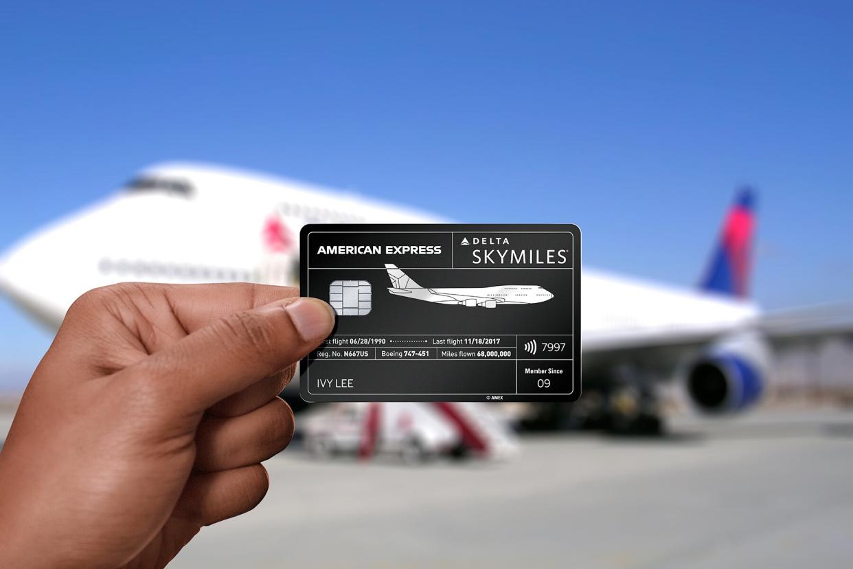 A hand holding the American Express x Delta, Consumer Reserve Card in front of a Delta airplane