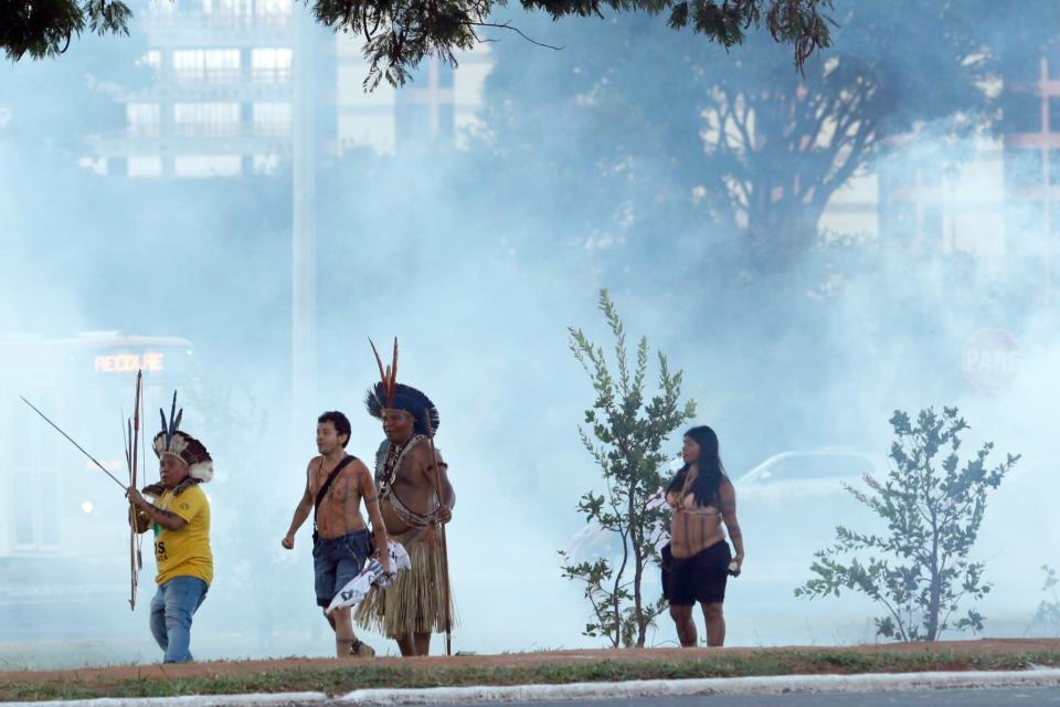 Protesters in traditional headdress points his bow and arrow towards the police