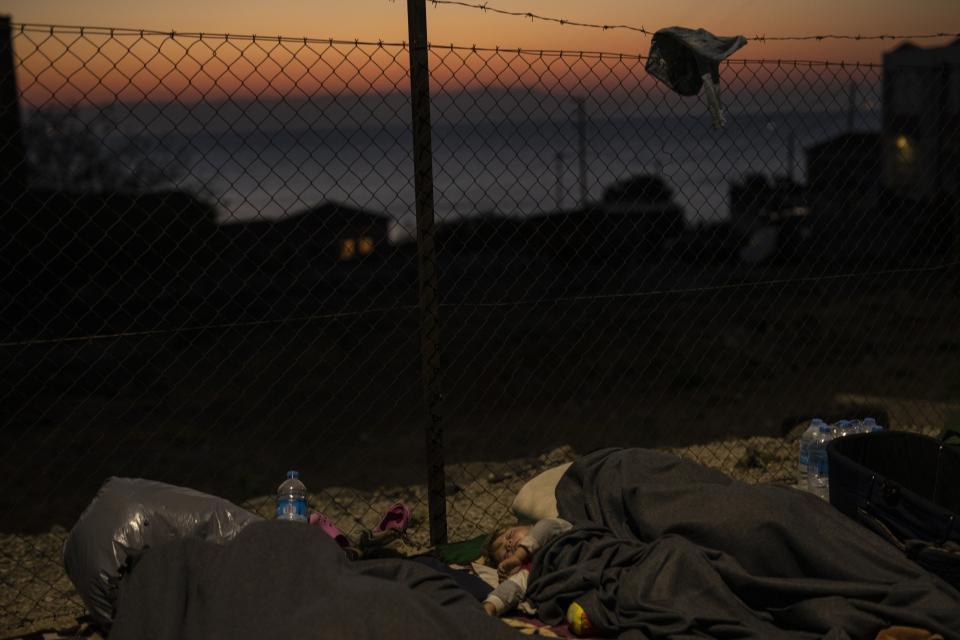 Migrants sleep on the roadside on the northeastern island of Lesbos, Greece, Friday, Sept. 11, 2020. The Greek government says thousands of migrants left homeless after fires gutted a sprawling refugee camp on the island of Lesbos will not be allowed to travel to mainland Greece. (AP Photo/Petros Giannakouris)