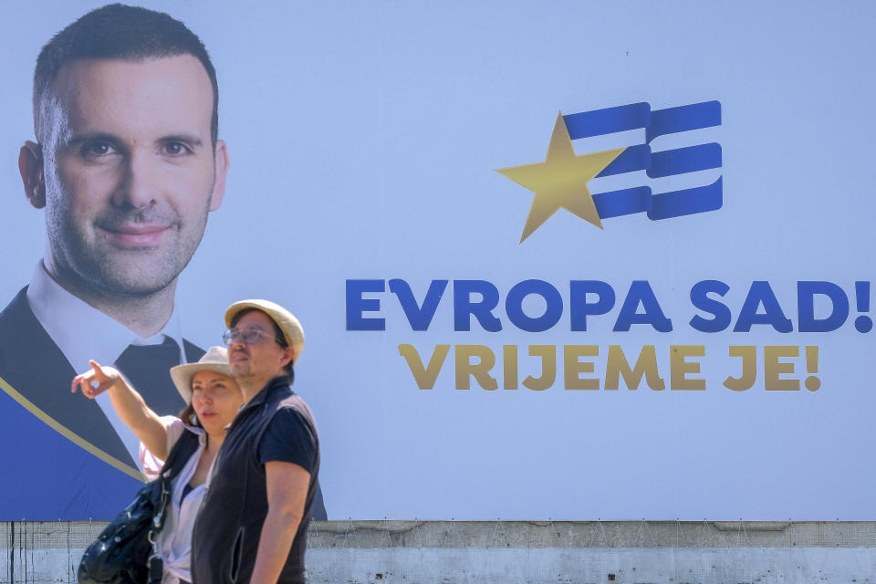 People walk past a pre-election billboard showing leader of the Europe Now movement, financial expert Milojko Spajic in Podgorica, Montenegro, Friday, June 9, 2023. Montenegro is holding an early parliamentary election Sunday, a vote that could provide indications of whether the small NATO member in the Balkans will overcome the deep political divisions and instability that have hampered its route to joining the European Union. (AP Photo/Risto Bozovic)