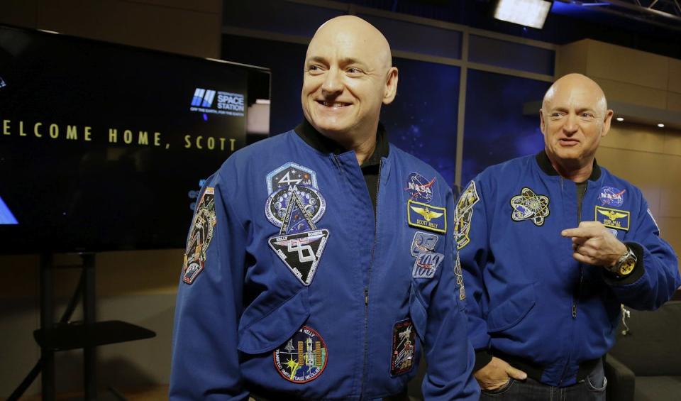 Two identical men wearing blue jumpsuits stand next to each other.