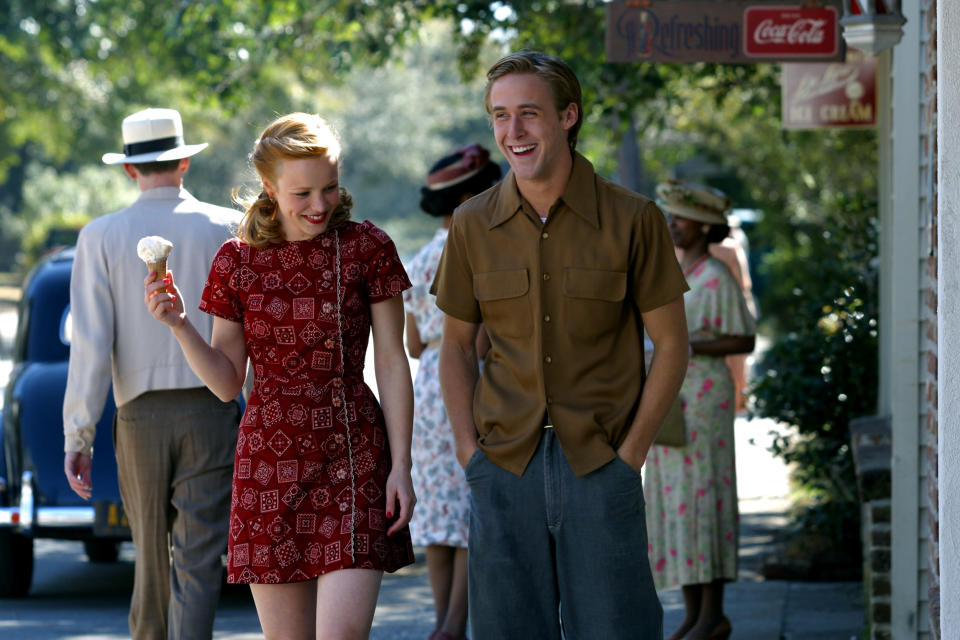 Rachel McAdams and Ryan Gosling walk together, smiling. McAdams is holding an ice cream cone and wearing a patterned dress, while Gosling wears a button-up shirt and pants in a scene from "The Notebook"