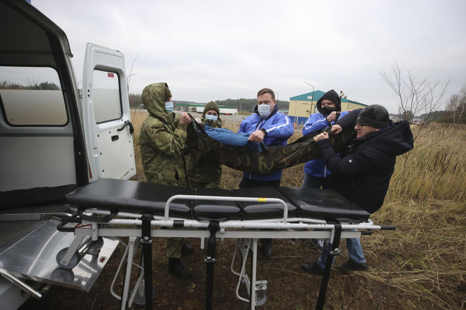 Belarusian volunteers transfer a sick person into an ambulance as other migrants gather at the Belarus-Poland border near Grodno, Belarus, Saturday, Nov. 13, 2021. A large number of migrants are in a makeshift camp on the Belarusian side of the border in frigid conditions. Belarusian state news agency Belta reported that Lukashenko on Saturday ordered the military to set up tents at the border where food and other humanitarian aid can be gathered and distributed to the migrants. (Leonid Shcheglov/BelTA pool photo via AP)