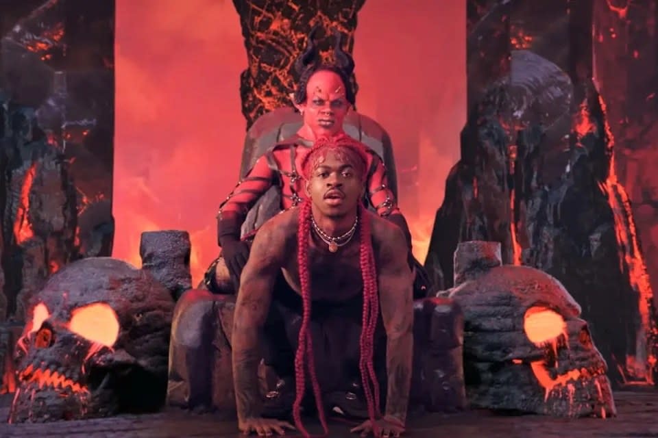 Lil Nas X giving a lap dance to someone dressed as the devil in a room with flaming red walls and giant skills