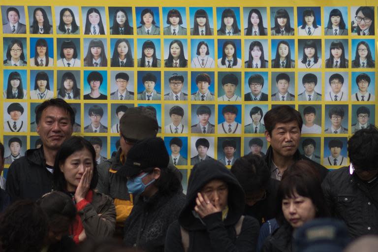 Relatives of victims of the Sewol ferry accident stand in front of a banner featuring photos of the victims, during a protest ahead of the anniversary of the disaster, in Seoul, on April 2, 2015