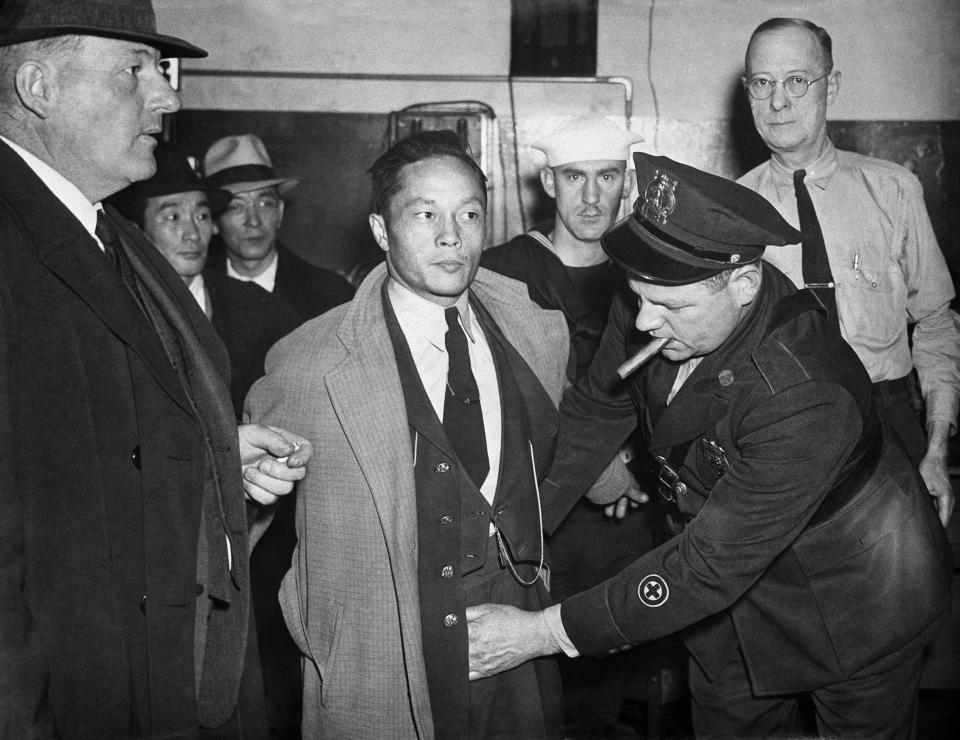 FILE - This Dec. 7, 1941 file photo shows a Japanese man under arrest in the roundup at Norfolk, Va., being searched by a policeman after Japan's declaration of war on the U.S. Beliefs that Hispanics and Asians living in the U.S. won't assimilate or refuse to speak English are based on stereotypes that scholars say are linked to notions of white supremacy. Throughout American history, Hispanics and Asians have been pressured to adopt the customs of the mainstream white population. The pressure came even as some laws forbade them from voting, intermarrying and having access to education and public facilities. (AP Photo, File)