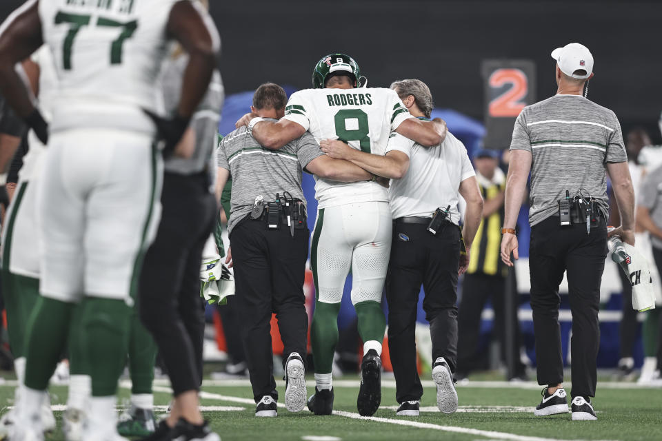 Aaron Rodgers stands between two people with their arms around him, apparently helping him walk.