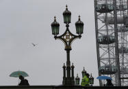 Tourists holding umbrellas pass a policeman standing on Westminster Bridge over the River Thames, with the London Eye in the background as rain falls in London, Thursday, Oct. 17, 2019. (AP Photo/Alastair Grant)