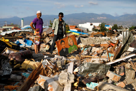 Two men recover a portrait of their dead parents from the rubble of their former house hit by an earthquake in Balaroa neighbourhood in Palu, Central Sulawesi, Indonesia, October 7, 2018. REUTERS/Jorge Silva