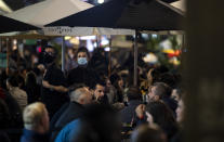 A waiter and waitress wearing masks serve their customers in the pedestrianized part of Old Compton Street in London, Friday, Oct. 23, 2020. In much of Europe, city squares and streets, be they wide, elegant boulevards like in Paris or cobblestoned alleys in Rome, serve as animated evening extensions of drawing rooms and living rooms. As Coronavirus restrictions once again put limitations on how we live and socialize, AP photographers across Europe delivered a snapshot of how Friday evening, the gateway to the weekend, looks and feels. (AP Photo/Alastair Grant)