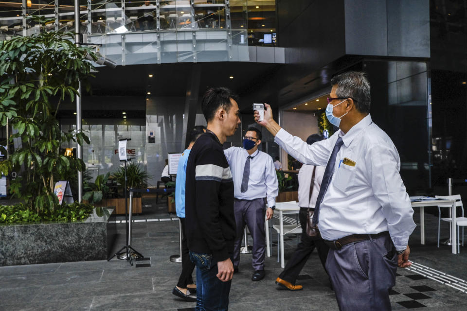 In this March 16, 2020, photo, a man scans a visitor's forehead to check his temperature before entering the Asia Square Tower in Singapore. As the virus outbreak spreads ever further, it's becoming clear that some strategies are more likely to succeed in containing it: pro-active efforts to track down and isolate cases, access to basic, affordable public health and clear, reassuring messaging from leaders. (AP Photo/Ee Ming Toh)