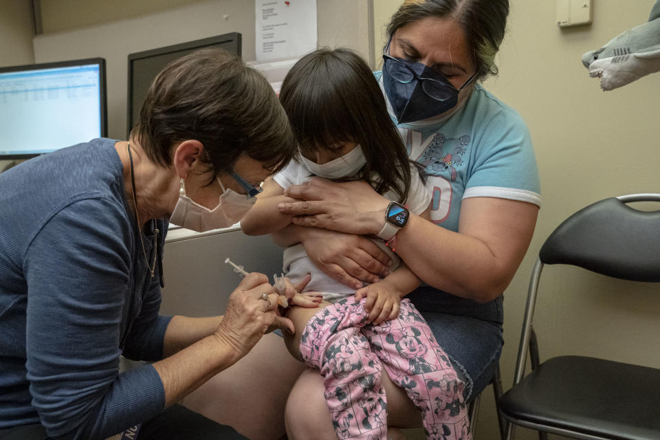 A nurse injects Deni Valenzuela, 2, who is sitting on her mother's lap, on the thigh.