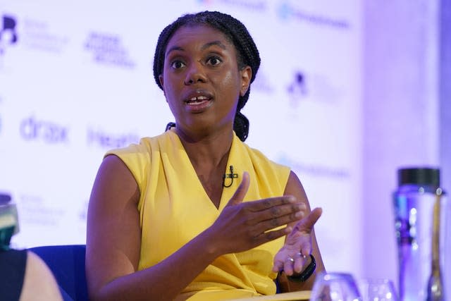 Kemi Badenoch on a purple lit stage wearing a yellow dress