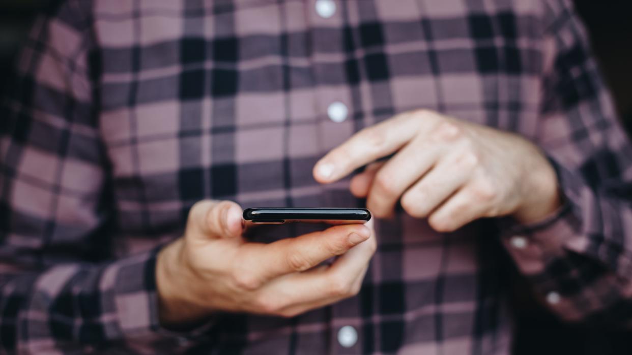  A close up on a man holding a phone and using it with one of his fingers. 