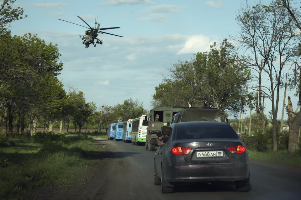 FILE - A Russian military helicopter flies over buses with Ukrainian servicemen evacuated from the besieged Mariupol's Azovstal steel plant traveling to a prison in Olyonivka, territory under the government of the Donetsk People's Republic, eastern Ukraine, Tuesday, May 17, 2022. Breaking its silence on prisoners of war, the Red Cross said Thursday, May 19, 2022 it has registered “hundreds” of Ukrainian prisoners of war who left the giant Azovstal steel plant in Mariupol after holding out in a weeks-long standoff with besieging Russian forces. (AP Photo/Alexei Alexandrov, File)