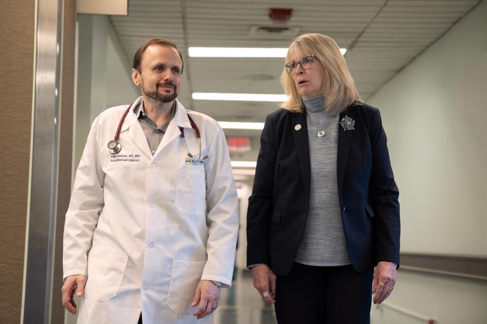 Barbara Piascik, an executive at Bergen New Bridge Medical Center has long COVID. She has been advised by Dr. Gian Varbaro, at left, the hospital's chief medical officer. Piascik and Varbaro talk as they walk down a hall at Bergen New Bridge Medical Center.