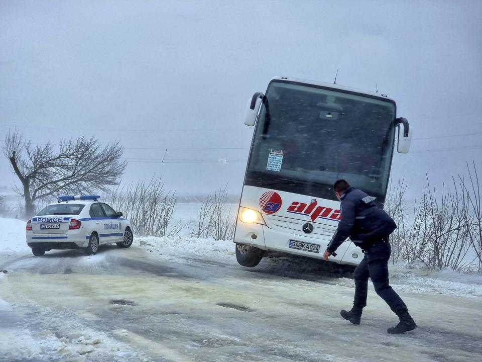 Policeman walks in front of a bus gone of the road near town of Dobrich, Bulgaria, Sunday, Nov. 19 2023. Gale-force winds and heavy rain and snow hit large parts of Bulgaria claiming the lives of two people and causing severe damages and disrupting power supply in towns and villages, officials said on Sunday. (Bulgarian News Agency via AP)