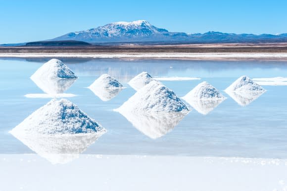 A lithium salt flat -- showing an evaporation pond with mountains and a blue sky in background.