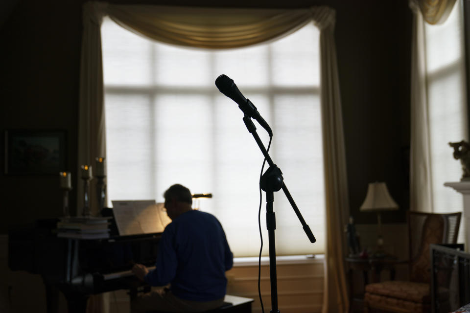 A microphone stands as David Lawyer plays the piano in his living room where his father, Neil Lawyer, would have sung along time to time in Bellevue, Wash., Sunday, March 20, 2022. The elder Lawyer died at age 84 on March 8, 2020, among the first residents of a Seattle area nursing home who succumbed to COVID-19 during the outbreak. At weddings, he joined his sons, grandson and nephew to serenade brides and grooms in a makeshift ensemble dubbed the Moose-Tones. Last October, when one of his granddaughters married, it marked the first family affair without Lawyer there to hold court. The Moose-Tones went on without him. "He would have just been beaming because, you know, it was the most important thing in the world to him late in life, to get together with family," David Lawyer says. "I can honestly tell you he was terribly missed." (AP Photo/David Goldman)