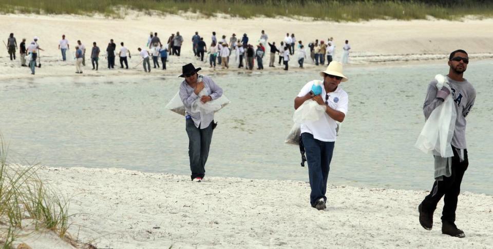 Workers carry bags of seagrass mixed with tar balls from a beach at St Andrews State Park in Panama City, June 21, 2010. The tar balls are suspected to be from the BP oils spill in the Gulf of Mexico. About eighty workers comb the beach to remove the tar balls that have been moving slowly eastward into waters off Florida.