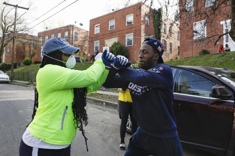 Inn this March 31, 2020, photo, volunteers India Blocker-Ford, left, with Indy B Mentoring, and Jimmie Jenkins, with ManPower DC, share a double elbow bump at the end of another long day delivering donated food to neighborhoods in southeast Washington. The direct to neighborhood deliveries are part of a new Martha's Table initiative, along with community partners, to get needed food directly to the neighborhoods they serve. Both Blocker-Ford and Jenkins grew up in DC's Ward 8. (AP Photo/Jacquelyn Martin)