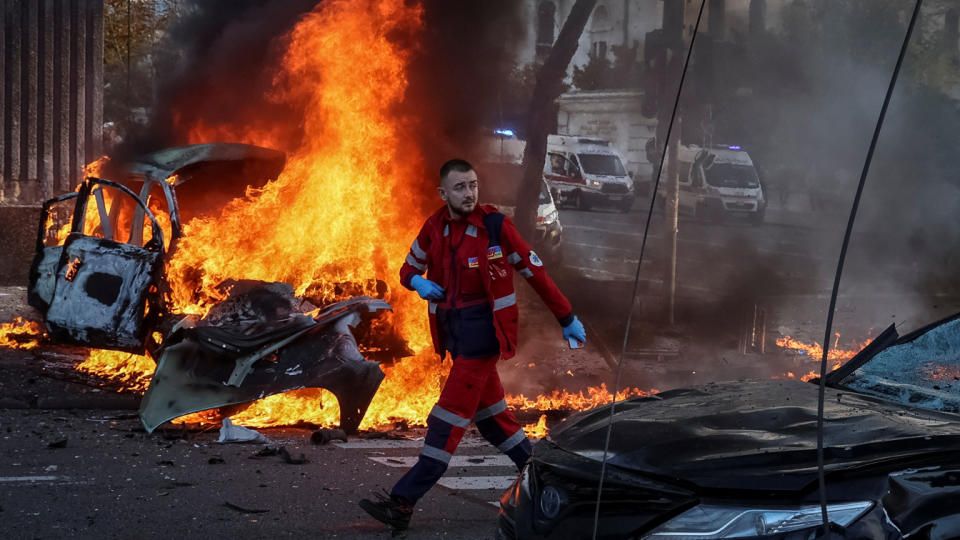 A medical worker walks past a burning car.