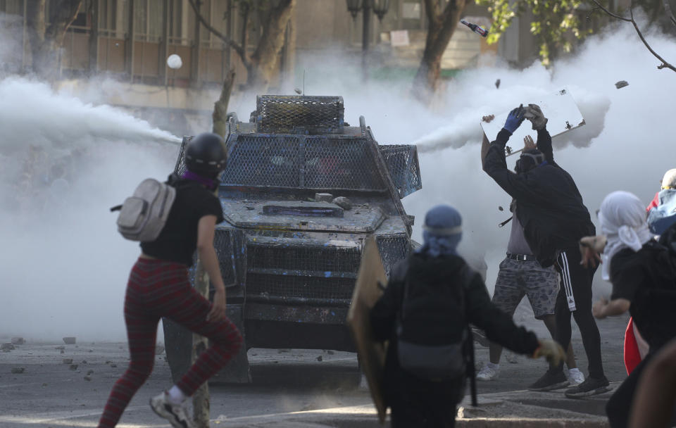 Anti-government demonstrators clash with a police armored vehicle spewing tear gas during protests in Santiago, Chile, Tuesday, Nov. 19, 2019. Chile has been facing weeks of unrest, triggered by a relatively minor increase in subway fares. The protests have shaken a nation noted for economic stability over the past decades, which has seen steadily declining poverty despite persistent high rates of inequality. (AP Photo/Esteban Felix)