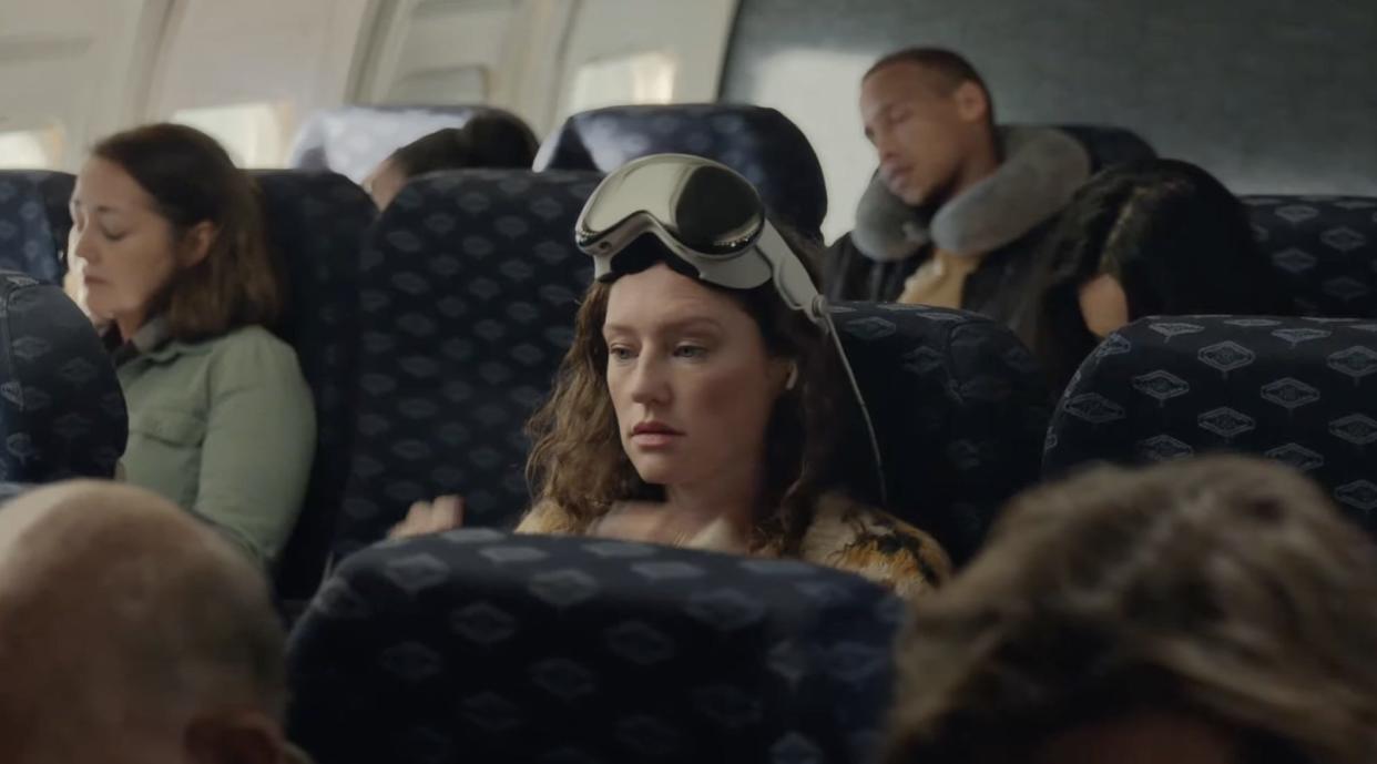 Woman seated in an airplane with Apple's Vision Pro on her head, like glasses.