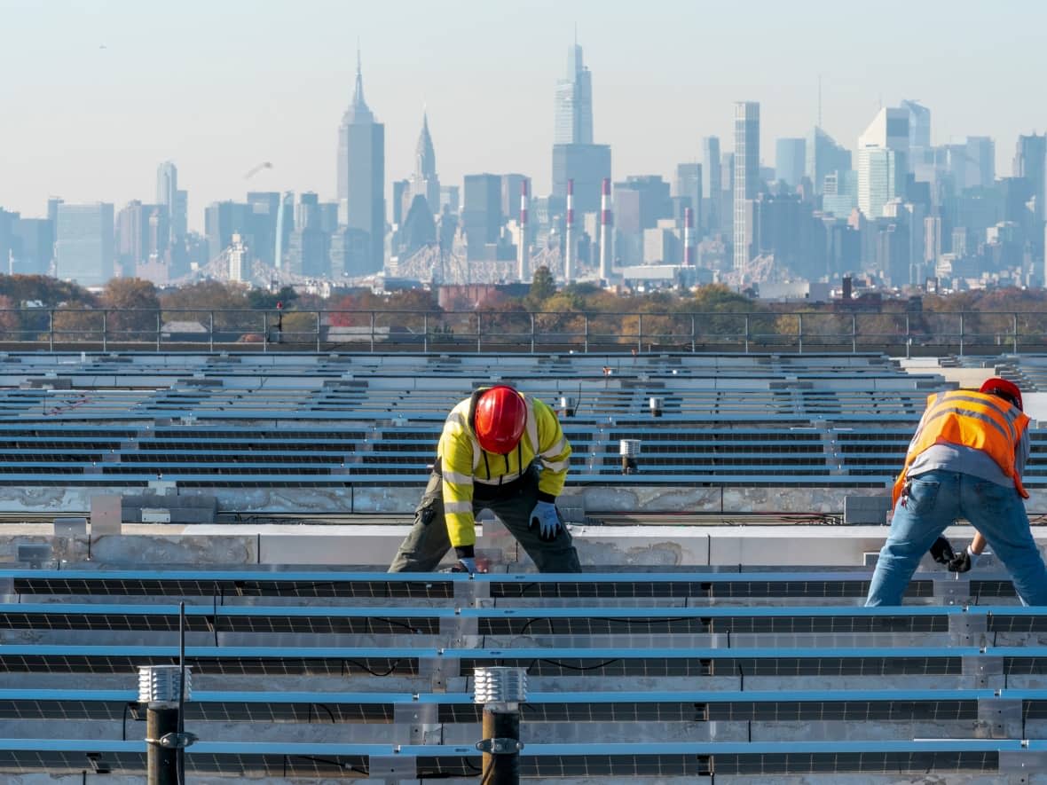 Electricians install solar panels on top of a garage at LaGuardia Airport in New York. U.S. lawmakers are hoping to pass a bill that would commit billions of dollars to solar installations and other clean energy projects. (Mary Altaffer/The Associated Press - image credit)