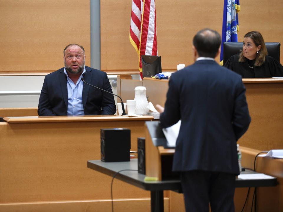 Infowars founder Alex Jones, left, is questioned by plaintiff's attorney Chris Mattei beside Judge Barbara Bellis, right, during testimony at the Sandy Hook defamation damages trial at Connecticut Superior Court in Waterbury, Conn. Thursday, Sept. 22, 2022.